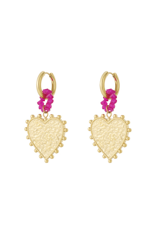 Pair of gold hoop earrings featuring textured heart-shaped pendants surrounded by ornamental dots and connected with bright pink beaded rings against white background