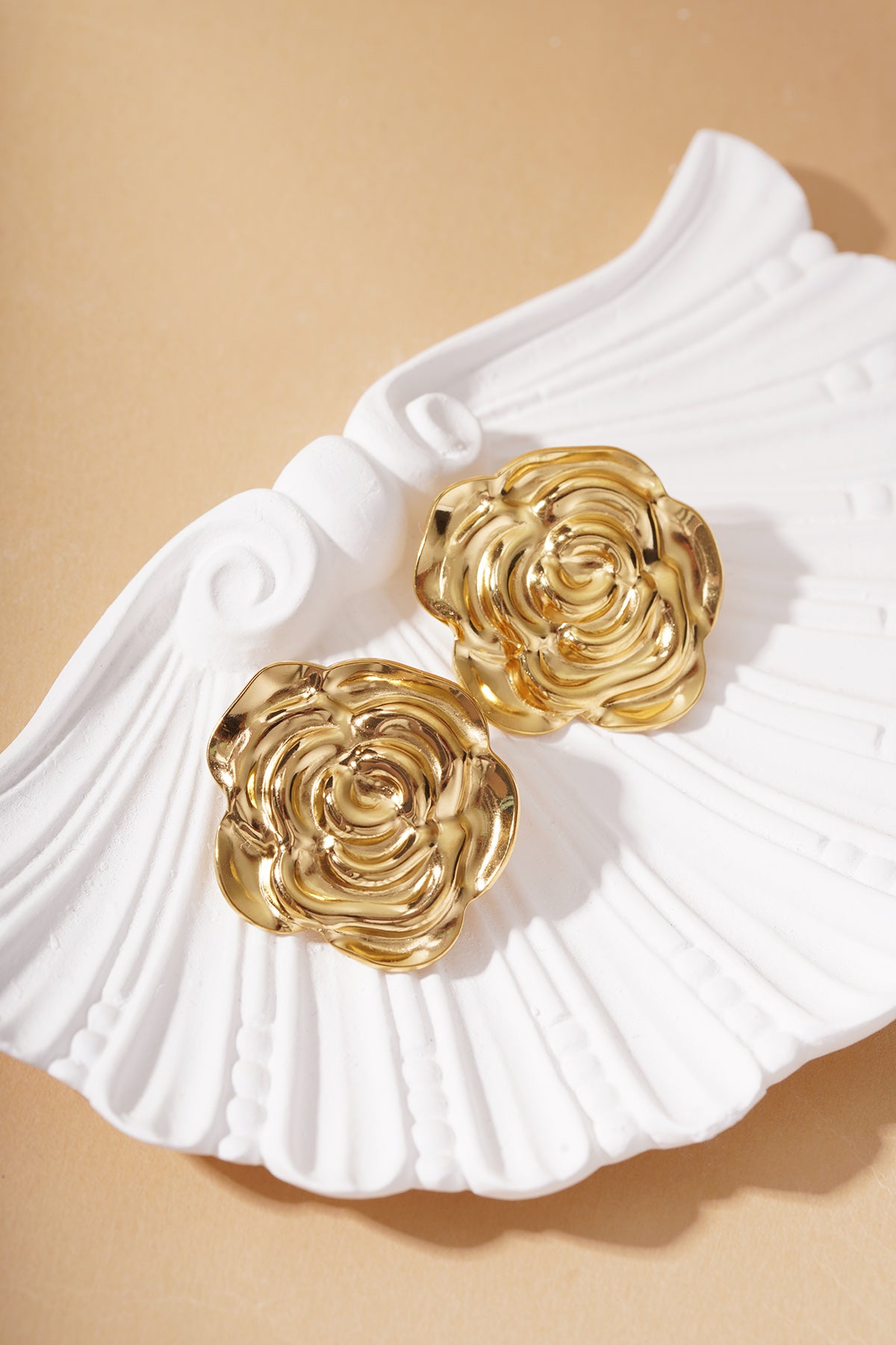 Bloom Core gold stud earrings shaped like blooming roses, resting on a white decorative shell-shaped dish.