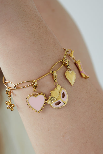 Close-up of the gold charm bracelet worn on a wrist showcasing the pink enamel heart and mask charms