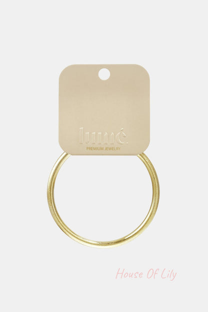 Simple gold-toned round bangle bracelet attached to a branded beige display card.