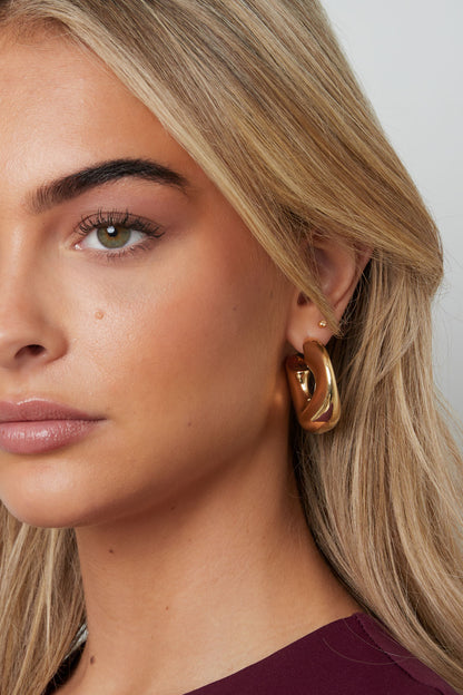 Close-up of a woman wearing chunky gold sculptural hoop earrings and a burgundy top