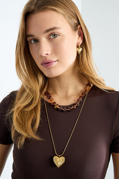 Woman wearing brown heart bead necklace with gold long pendant necklace and gold heart earrings