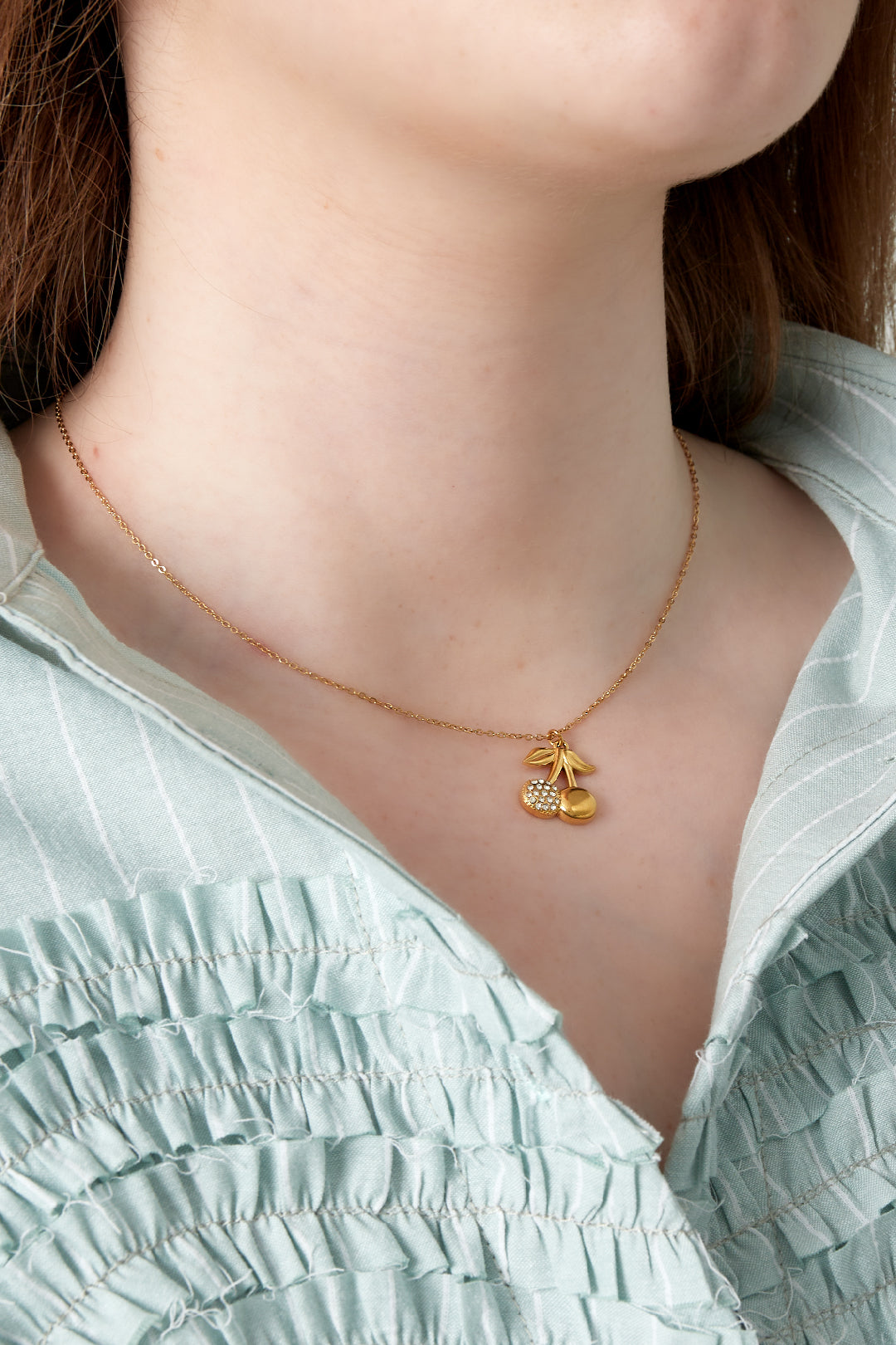 Close-up of a woman wearing the gold cherry pendant necklace with rhinestones, styled with a light green blouse