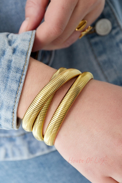 Close-up of woman’s wrist wearing gold-tone triple coil wrap bracelet against denim jacket