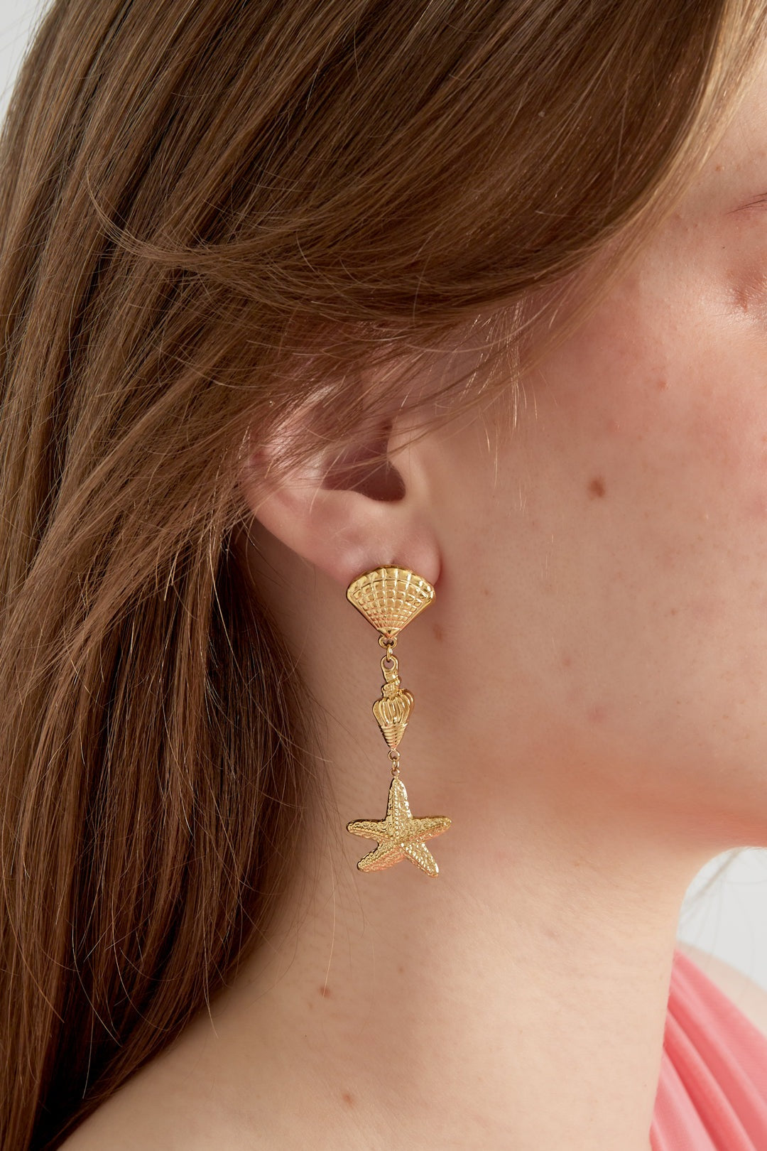 Model wearing gold sea life themed dangle earrings showing size and fit on ear