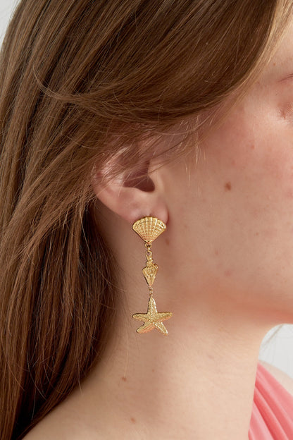 Model wearing gold sea life themed dangle earrings showing size and fit on ear