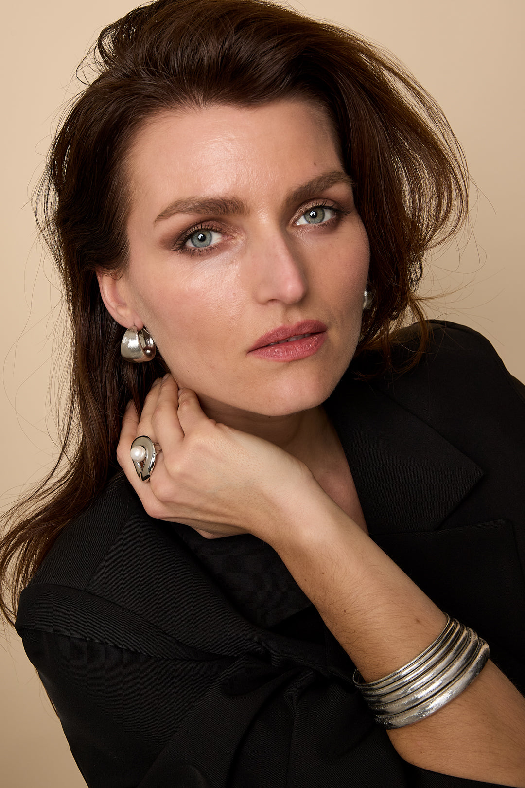 Model wearing silver textured chunky hoop earrings, silver ring with pearl, and silver metal bracelets
