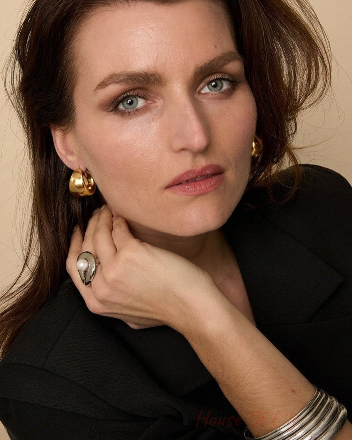 A woman wears chunky gold hoop earrings, a silver ring with a pearl, and stacked silver bracelets.