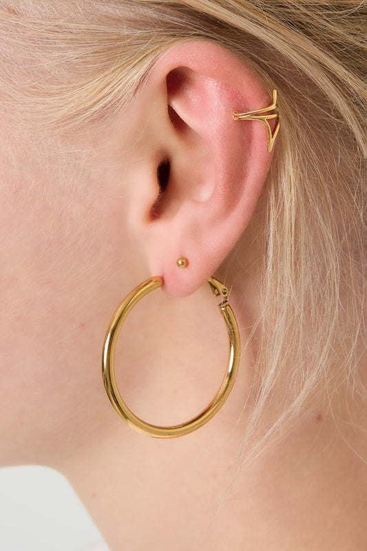 Close-up of gold hoop earring worn on ear with additional gold ear cuff and stud