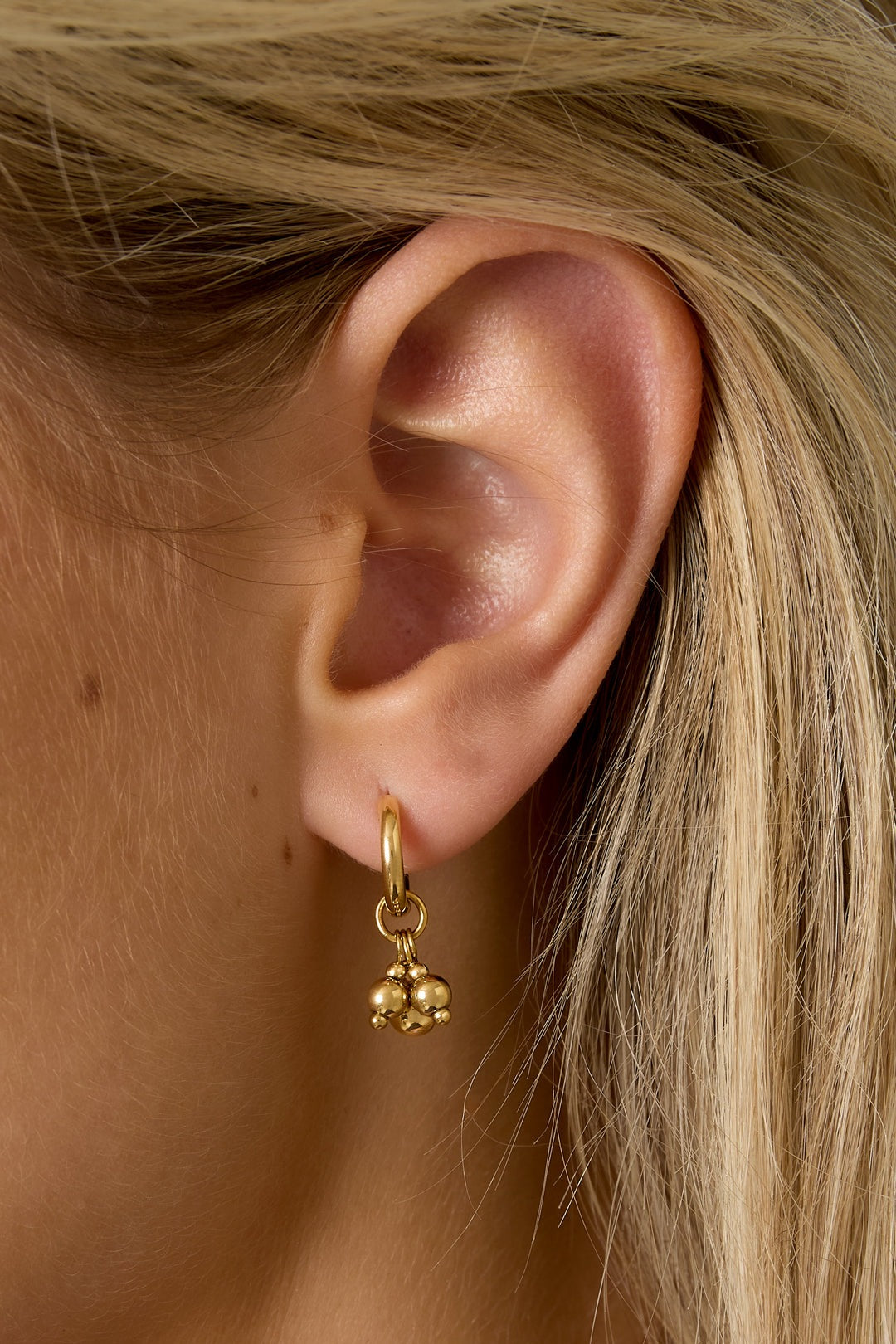 Close-up view of a woman's ear wearing a gold hoop earring with three dangling spheres