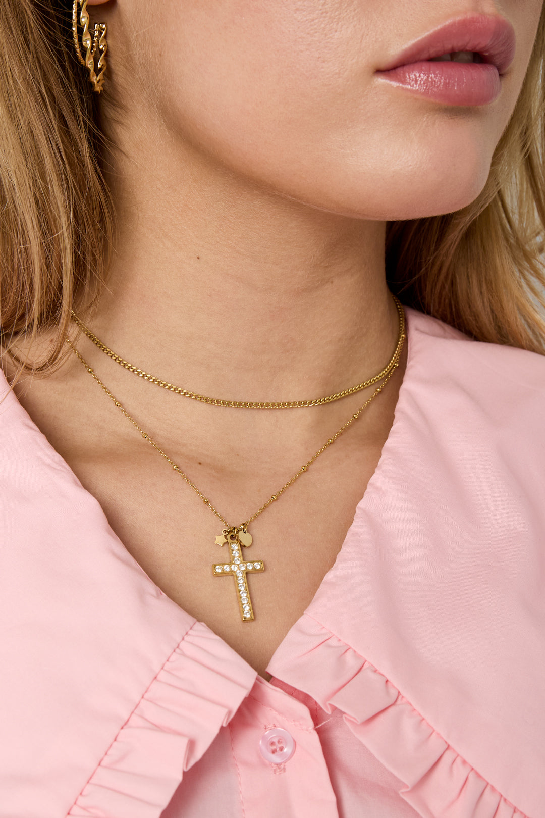 Gold-toned layered necklace featuring a Y2K-style cross pendant adorned with small crystals, worn on a model.