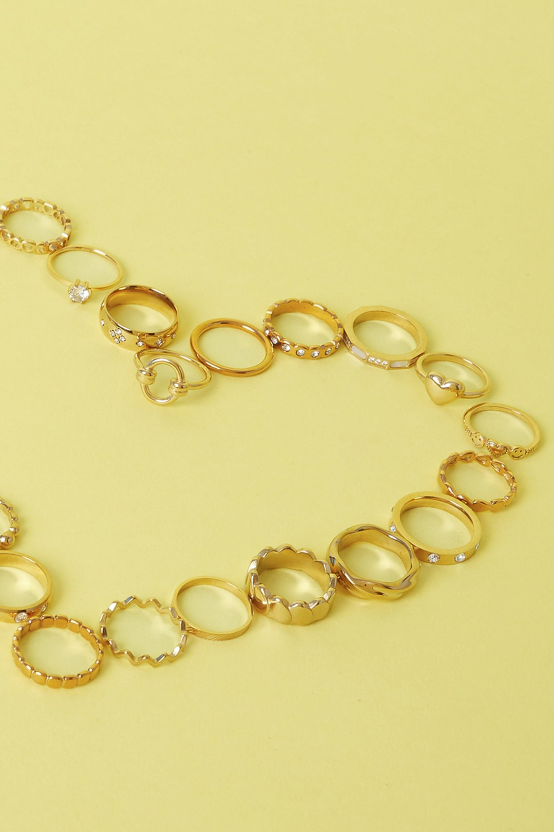 Collection of various gold rings with different textures and designs placed on a yellow surface
