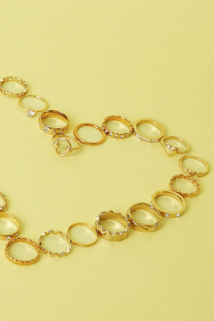 Collection of various gold rings with different textures and designs placed on a yellow surface