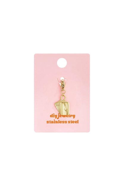 Gold Cards Era charm pendant on pink display card, featuring a miniature hand of playing cards in stainless steel.