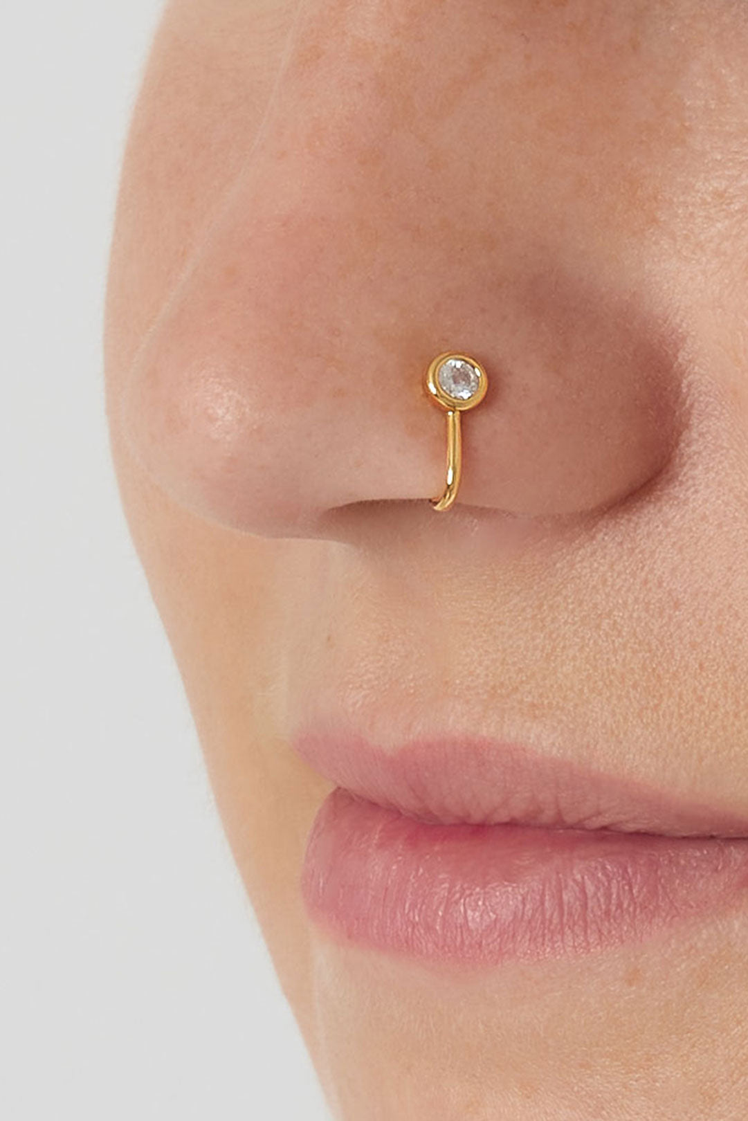 Close-up of a gold zircon nose cuff worn on a woman's nose, showing minimalist and soft design