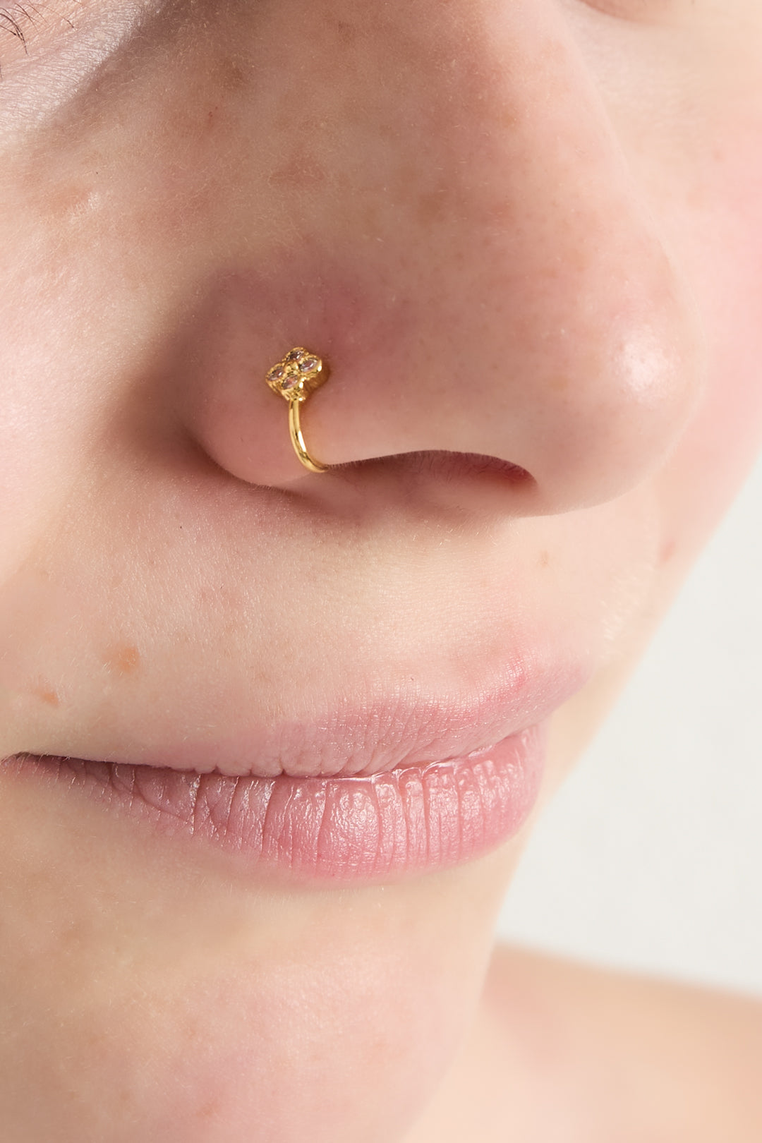 Close-up of a woman wearing the gold zircon clover and heart nose cuff on her nostril