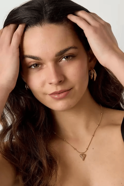 Model wearing a gold Chiseled Heart Core pendant on a delicate beaded chain necklace against a white background.