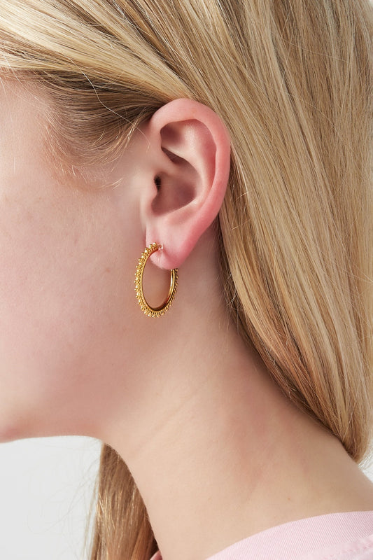 Close-up side profile of woman wearing gold beaded edge clip-on hoop earring