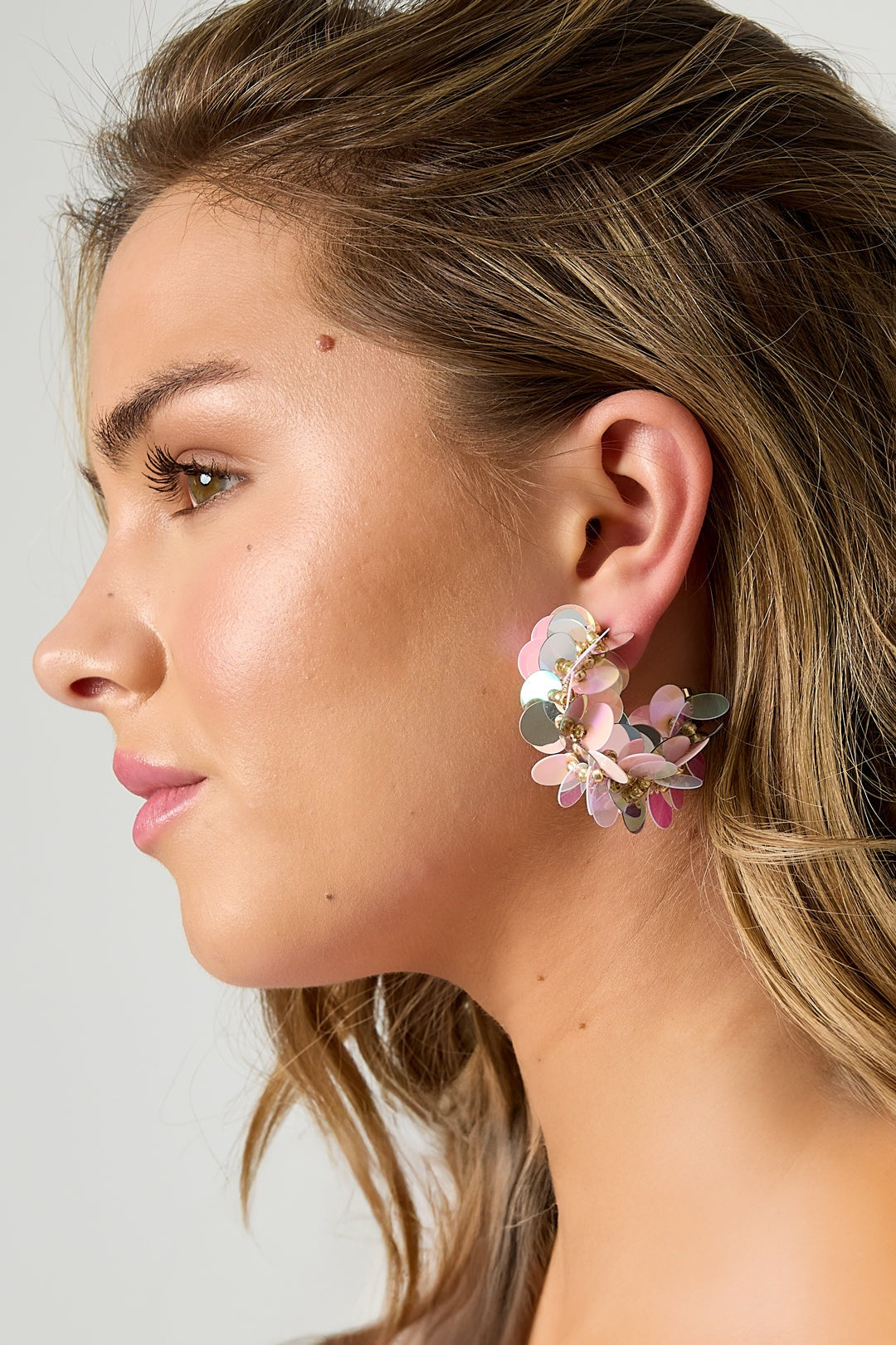 Close-up side view of pink and silver iridescent sequin hoop earring on model's ear