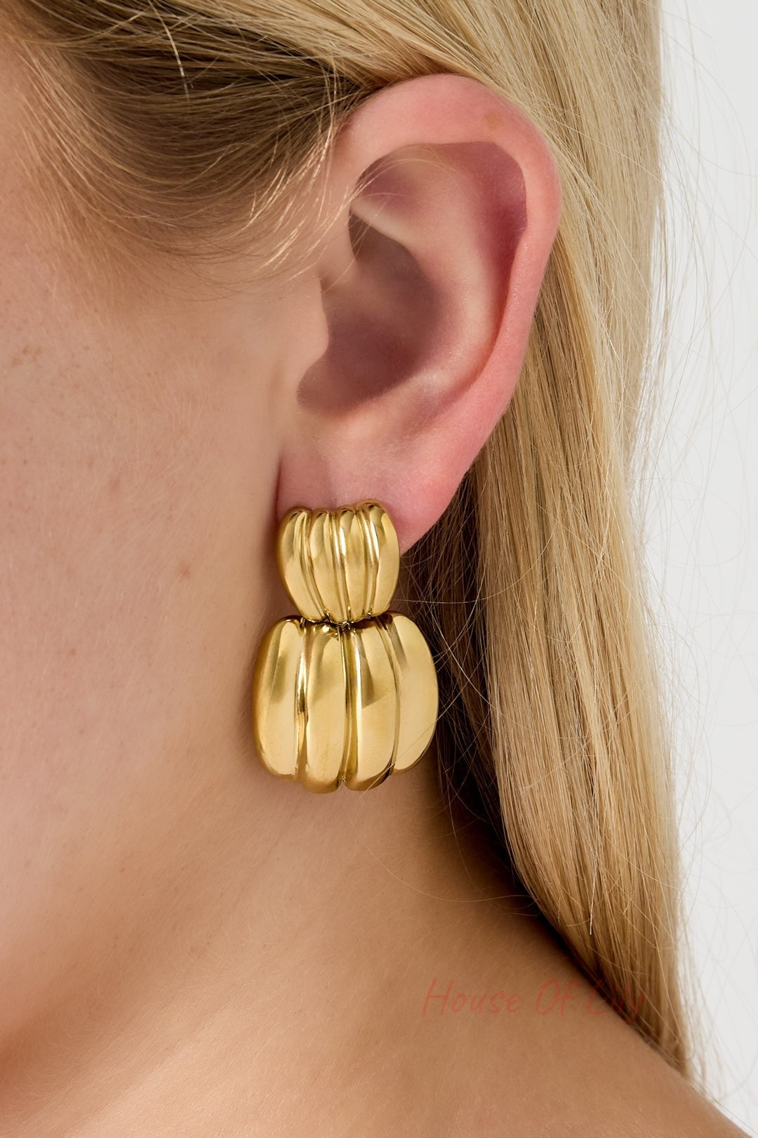 Gold chunky hoop earring worn on a woman’s ear showcasing its size and shine