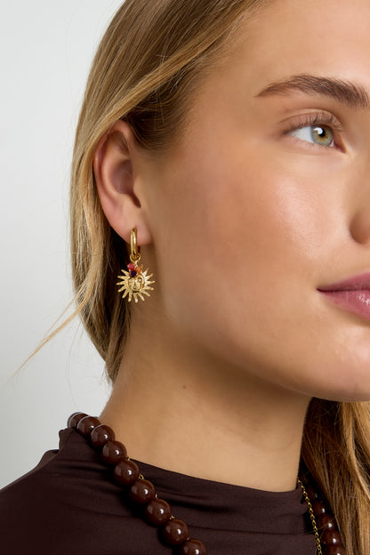 Close-up of a woman wearing gold sun charm hoop earring with amber beads styled with brown beaded necklace and dark brown top