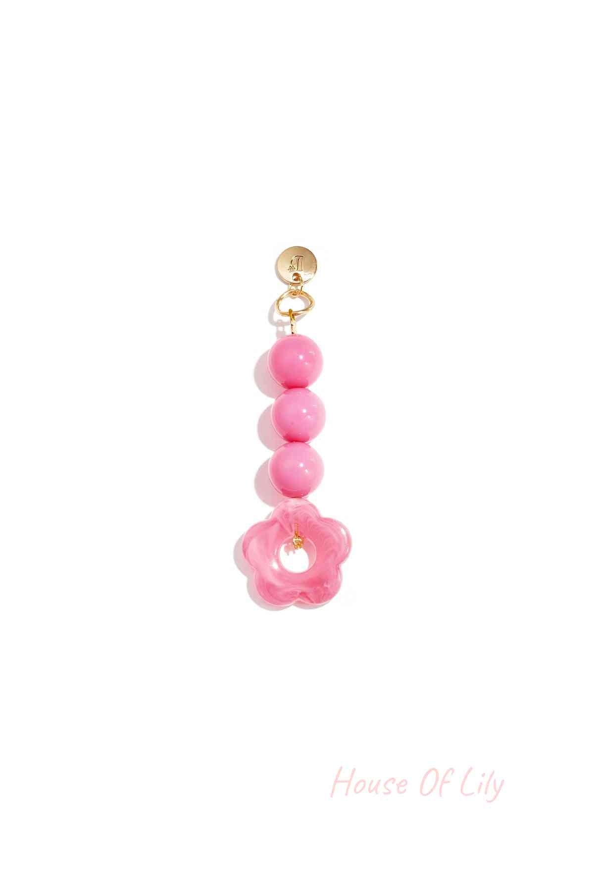 Pink acrylic flower bag charm with three round beads hanging from a gold clasp on white background