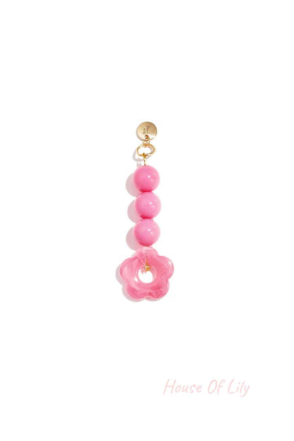 Pink acrylic flower bag charm with three round beads hanging from a gold clasp on white background
