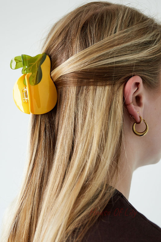 Model wearing yellow pear-shaped hair claw clipped into blonde hair, showing the accessory and gold hoop earrings