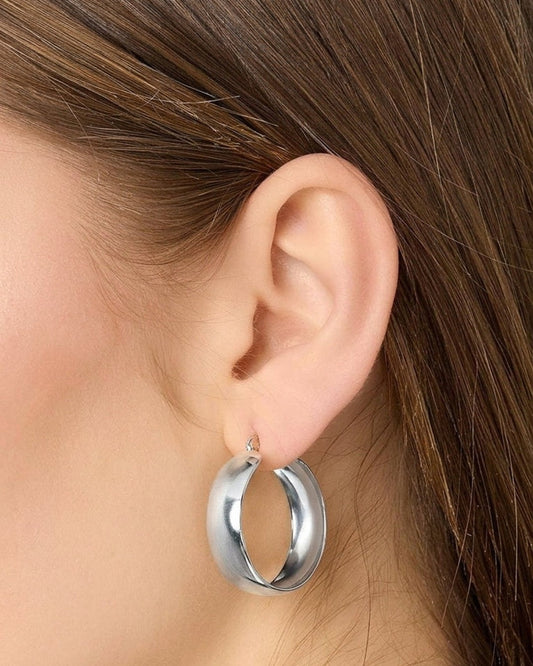 Shiny silver, thick, chunky hoop earrings worn on a woman's ear. Minimalist House of Lily design.