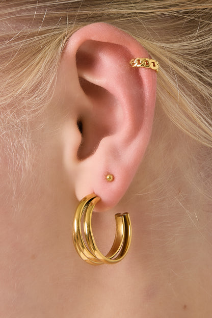 Model wearing a gold chunky chain ear cuff on the upper ear, paired with gold hoop earrings and a tiny gold stud.