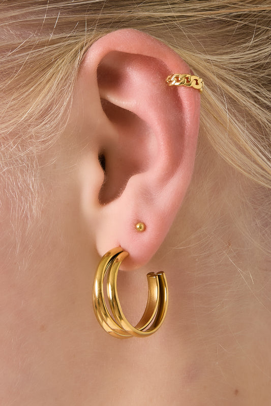 Model wearing a gold chunky chain ear cuff on the upper ear, paired with gold hoop earrings and a tiny gold stud.