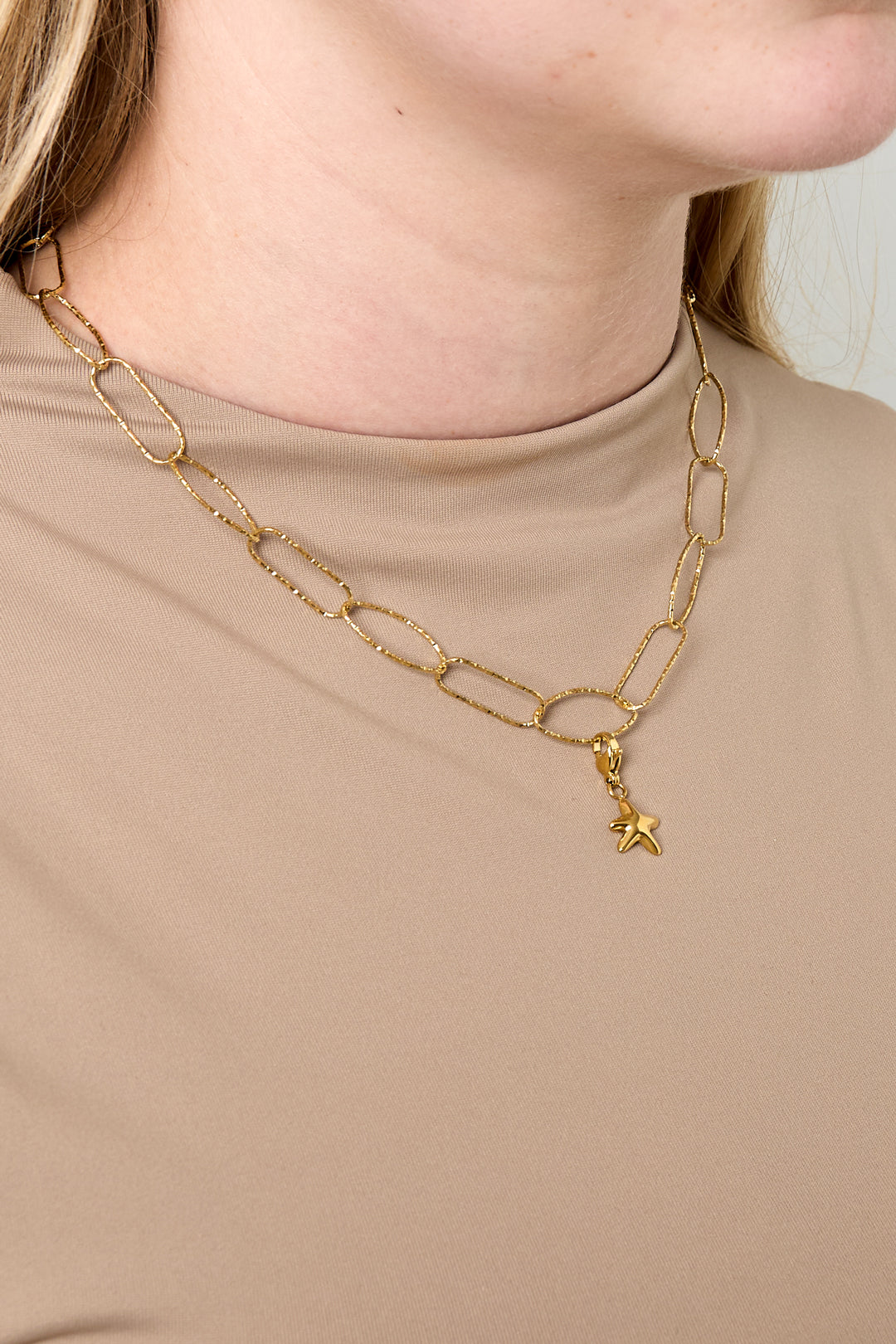 Model wearing gold paperclip chain necklace with small star charm paired with beige top