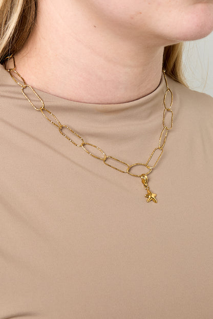 Model wearing gold paperclip chain necklace with small star charm paired with beige top