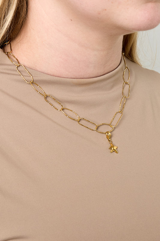 Model wearing gold paperclip chain necklace with small star charm paired with beige top
