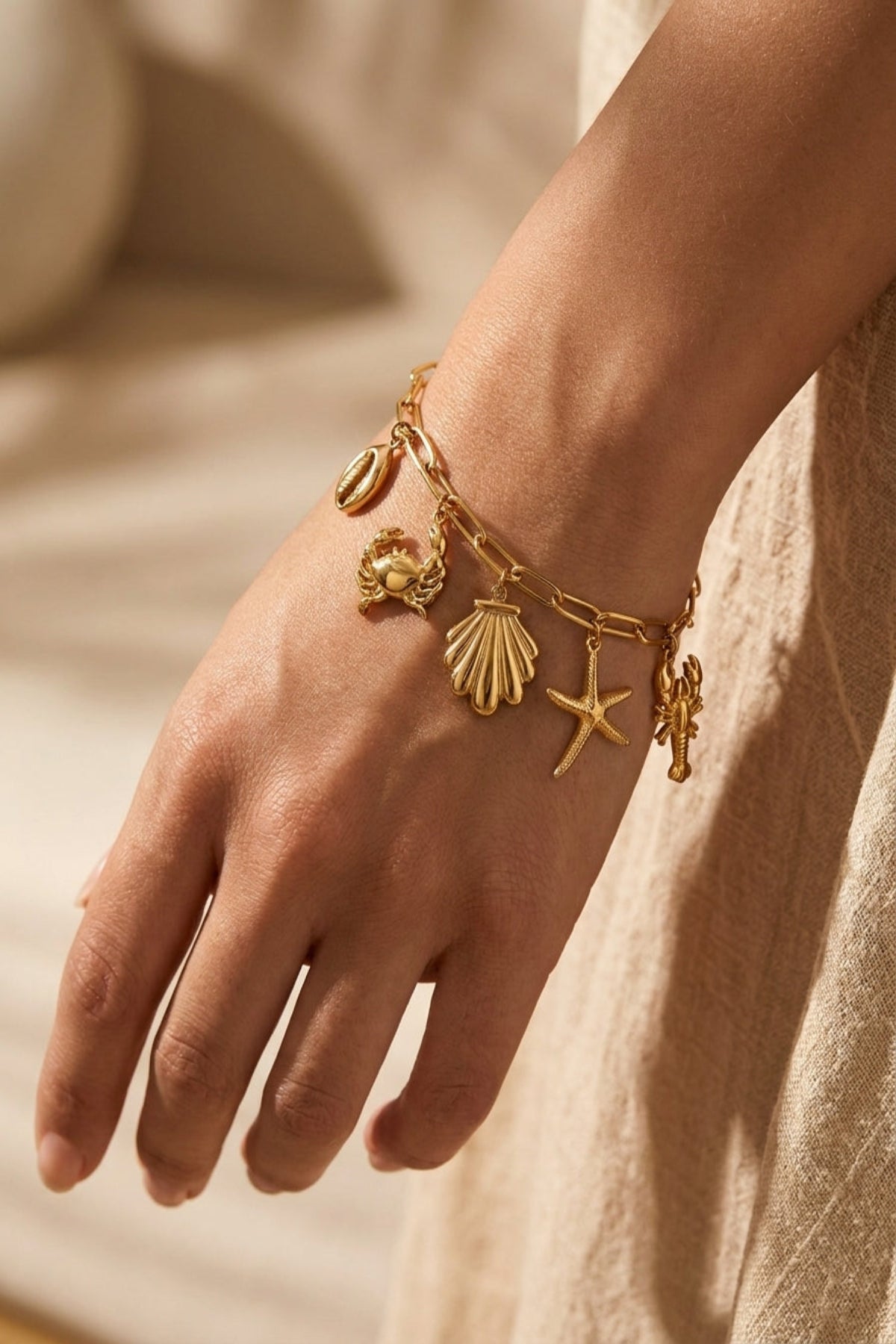 Gold bracelet with shell and starfish charms on a wrist against a neutral background