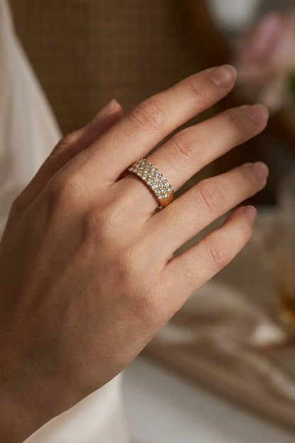A wide gold band ring featuring three rows of pavé rhinestones, worn on a hand.
