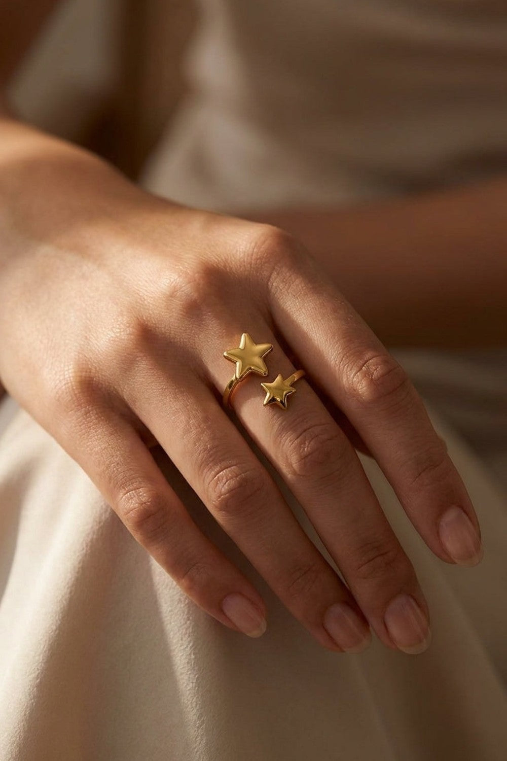 A gold minimalist ring featuring two asymmetrical star motifs on an open band, worn on a hand.