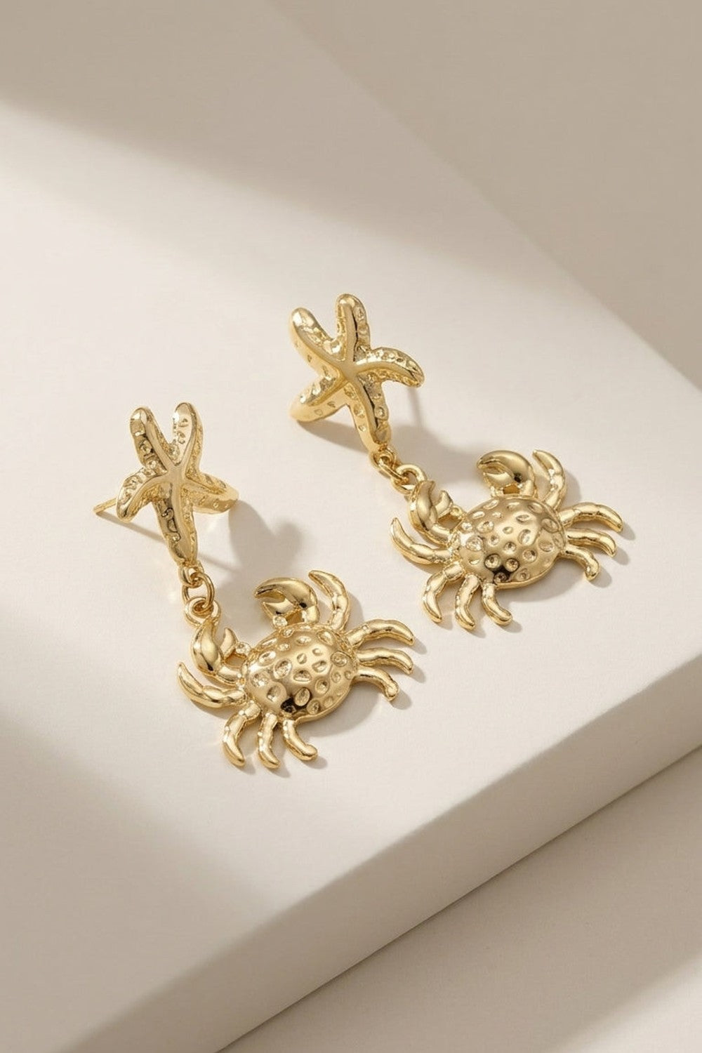 Gold drop earrings featuring a starfish stud dangling a textured crab pendant.