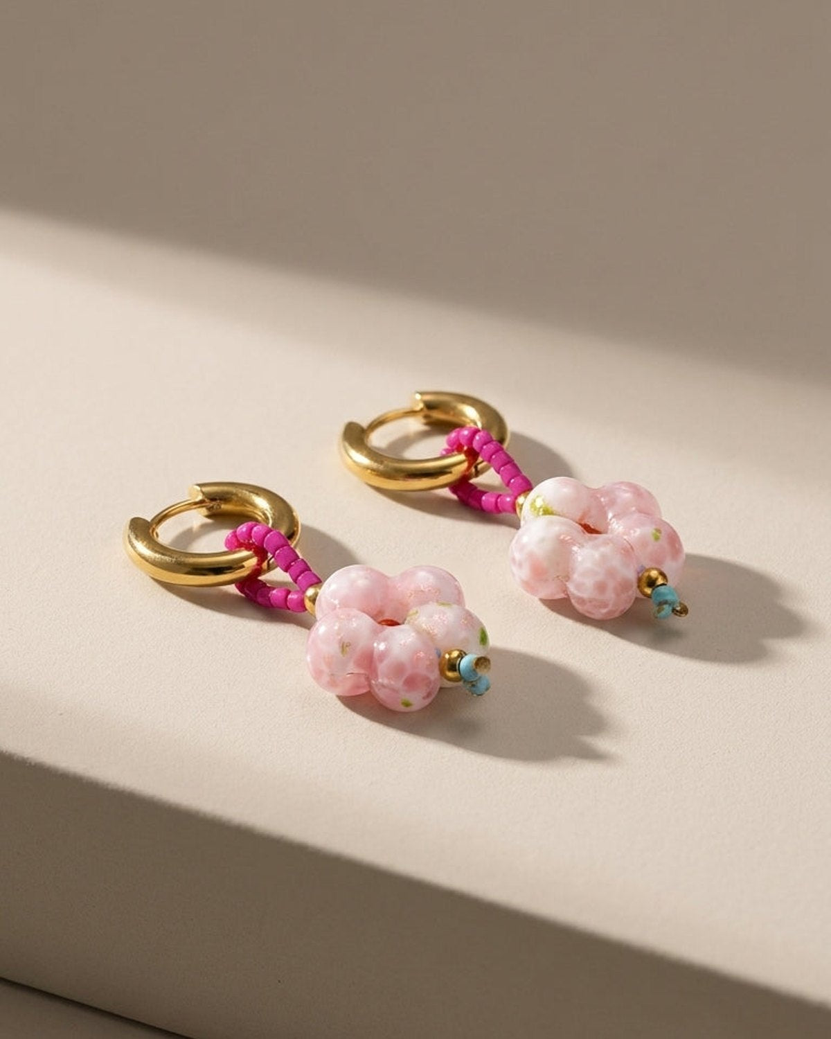 Gold hoop earrings with pink beaded loops and pink patterned flower-shaped glass bead drops.