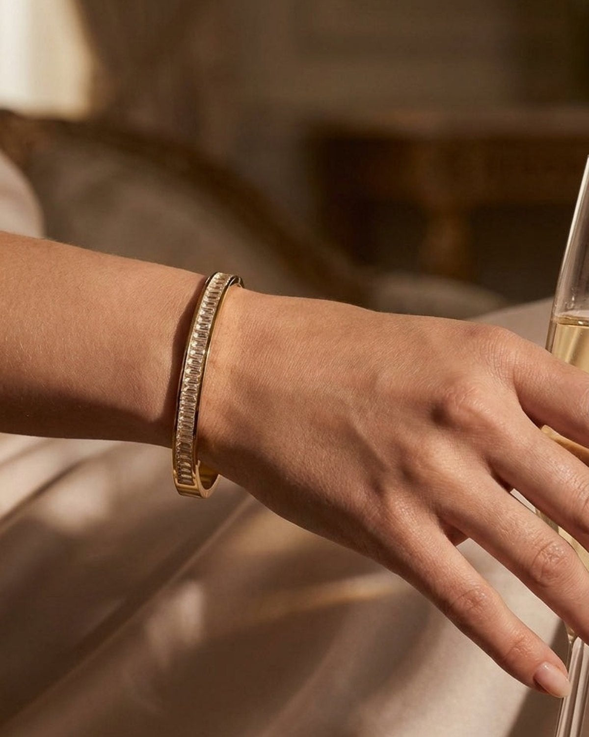 Gold-toned metal bangle bracelet encrusted with vertical baguette-cut clear crystals on a wrist.