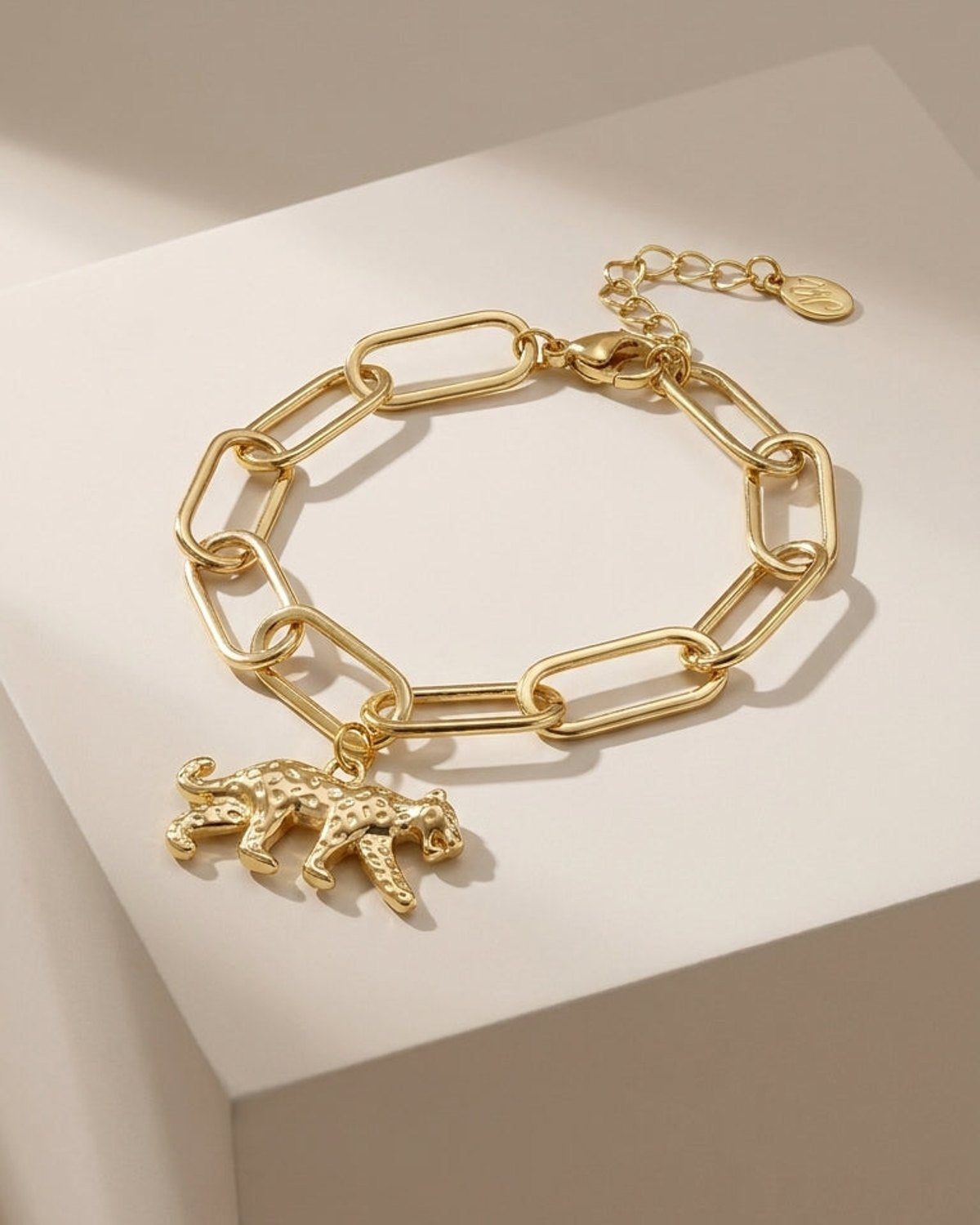 Gold chain link bracelet with a spotted leopard charm hanging from it.