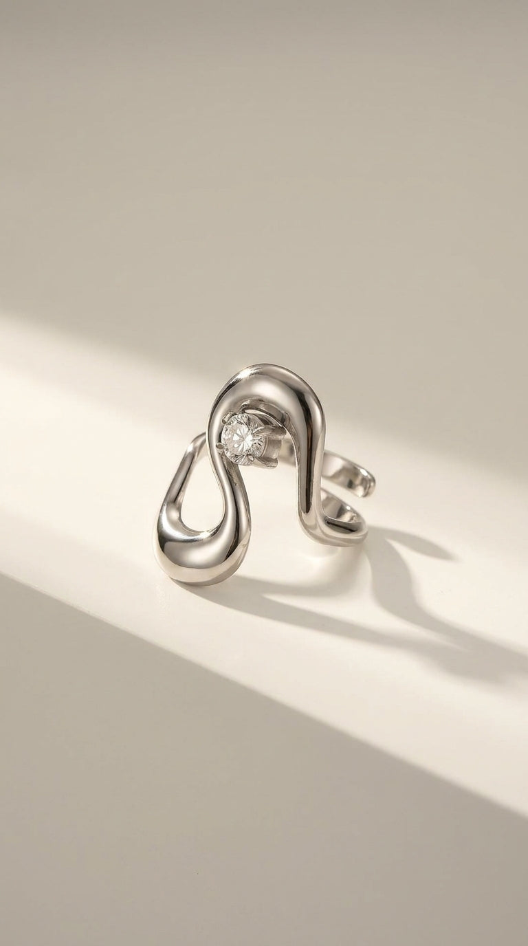 Irregular silver statement ring with an asymmetric, fluid loop design holding a single round gemstone.
