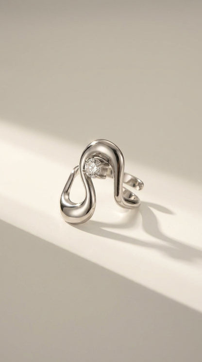 Irregular silver statement ring with an asymmetric, fluid loop design holding a single round gemstone.