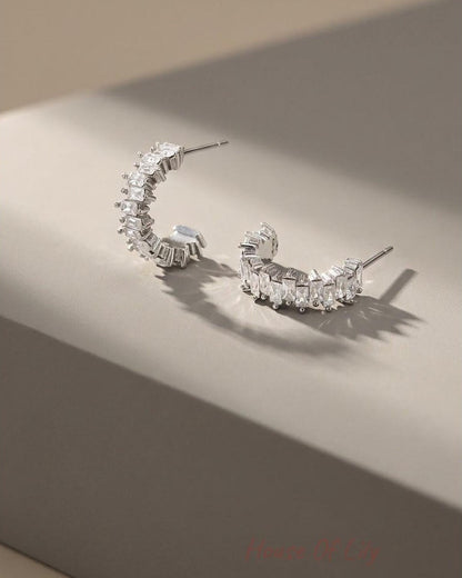 Silver hoop earrings featuring a zigzag arrangement of clear rectangular baguette stones.
