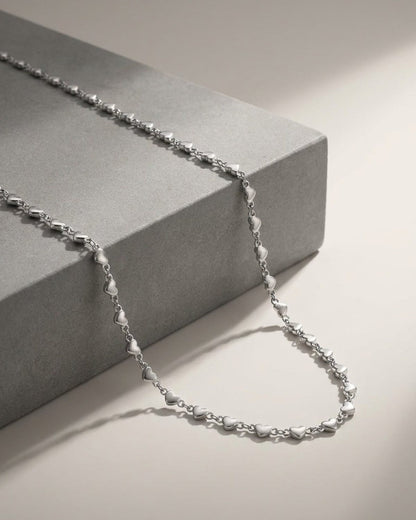 Delicate silver chain necklace featuring multiple small heart charms, draped over a grey block.