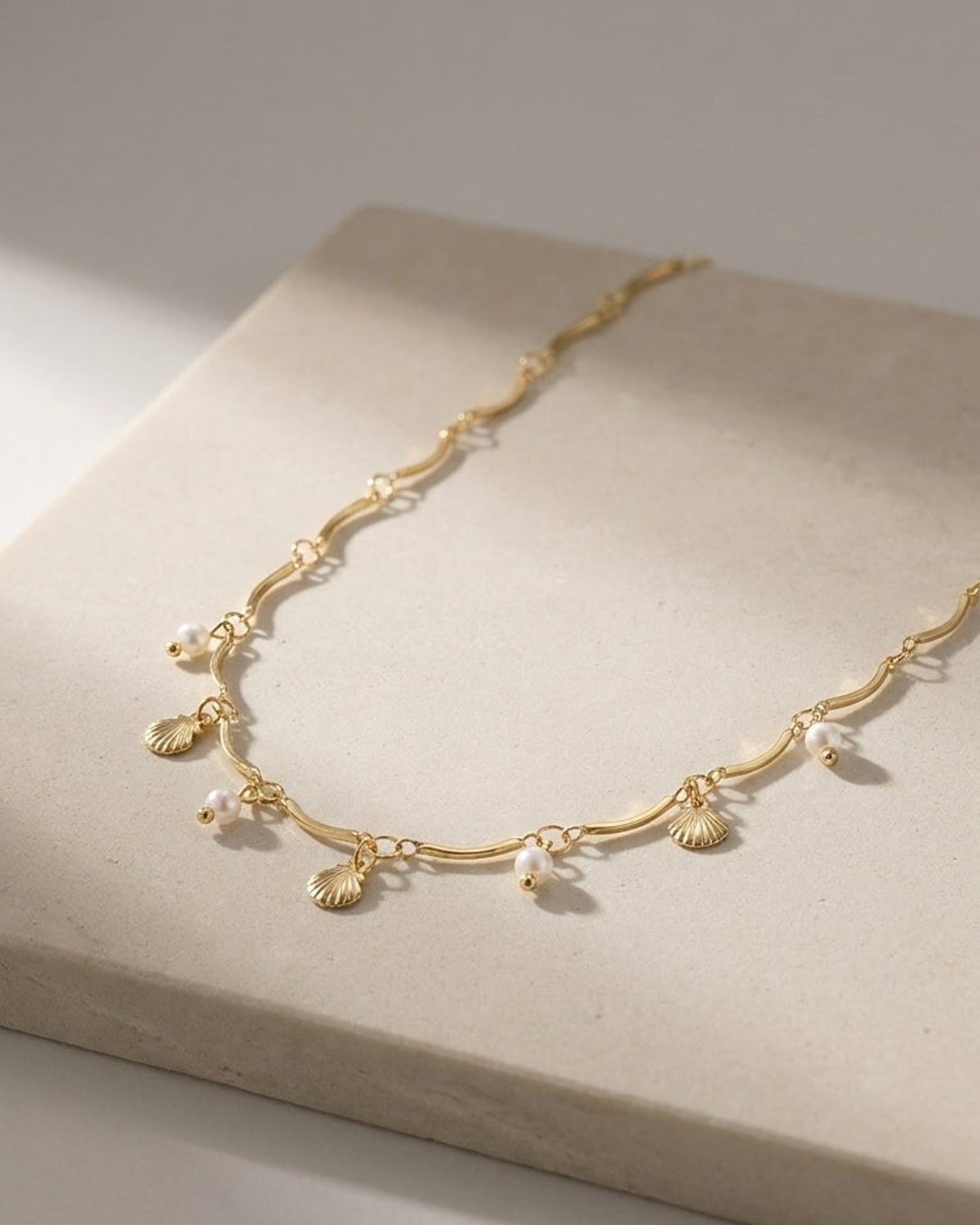 Gold wave-link necklace featuring dangling seashell charms and small white pearls.