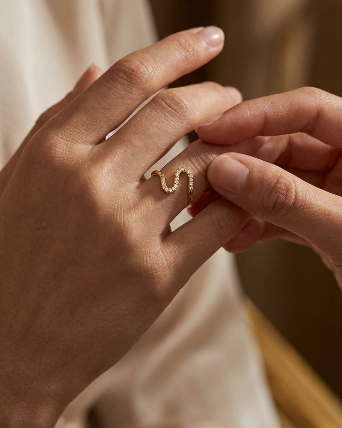 A gold Rhinestone Line Ring with a wavy, serpentine design embedded with sparkling rhinestones on a finger.