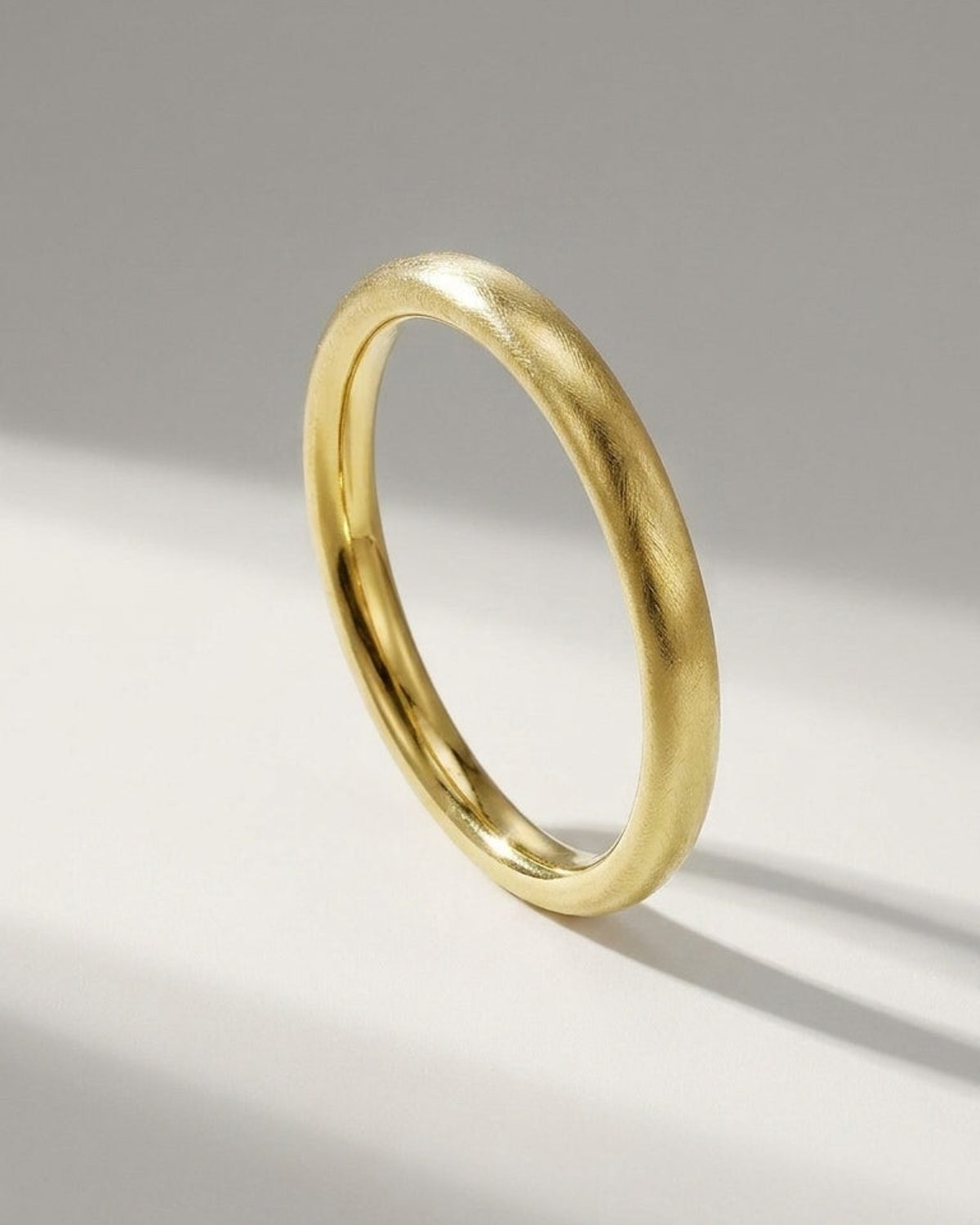 A gold-colored bangle with a brushed, textured finish and a rounded profile, resting on a white surface.