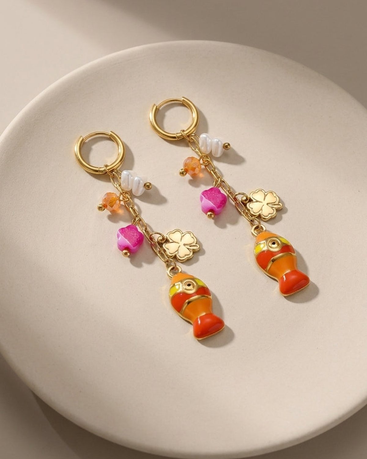 Gold hoop earrings with charms including enamel orange fish, pink flowers, clover, and pearls.