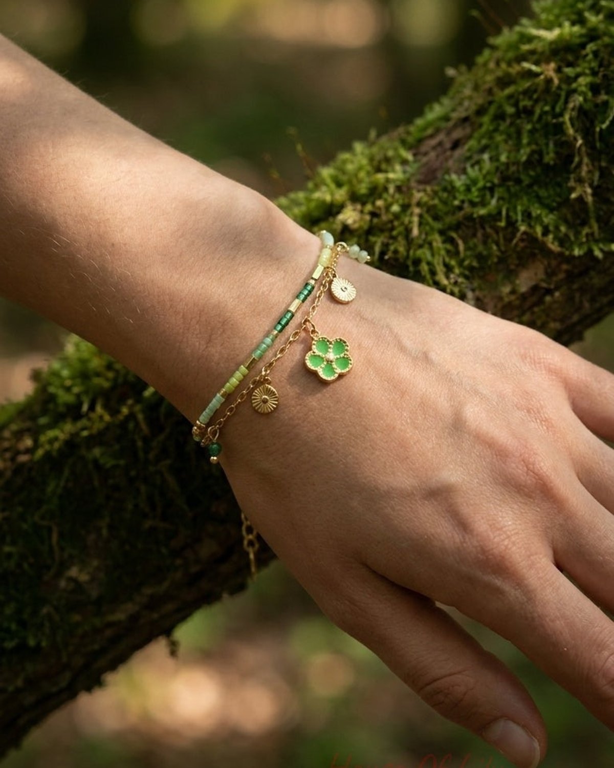 Gold chain charm bracelet with green enamel flower and sun charms, paired with a green seed-bead bracelet.